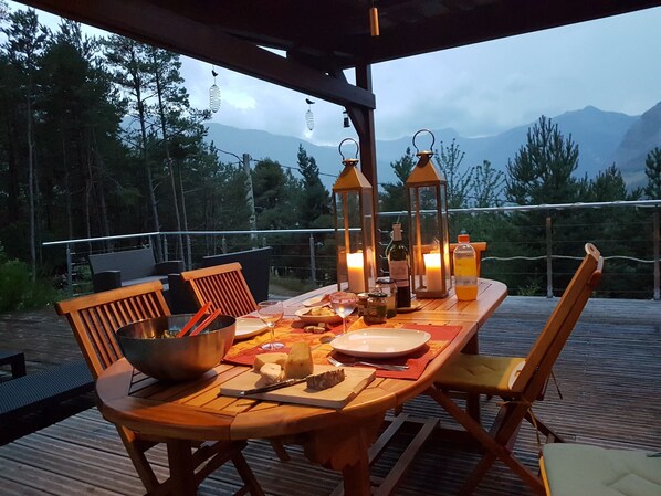 Eine Holzterrasse mit Esstisch und Stühlen, mit Blick auf eine gebirgige Landschaft.