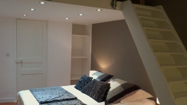 A bedroom with a bed, a nightstand, a white door, and a staircase.