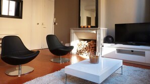 A modern living room with two black chairs, a white coffee table, a flat-screen TV, a fireplace, and a large mirror.