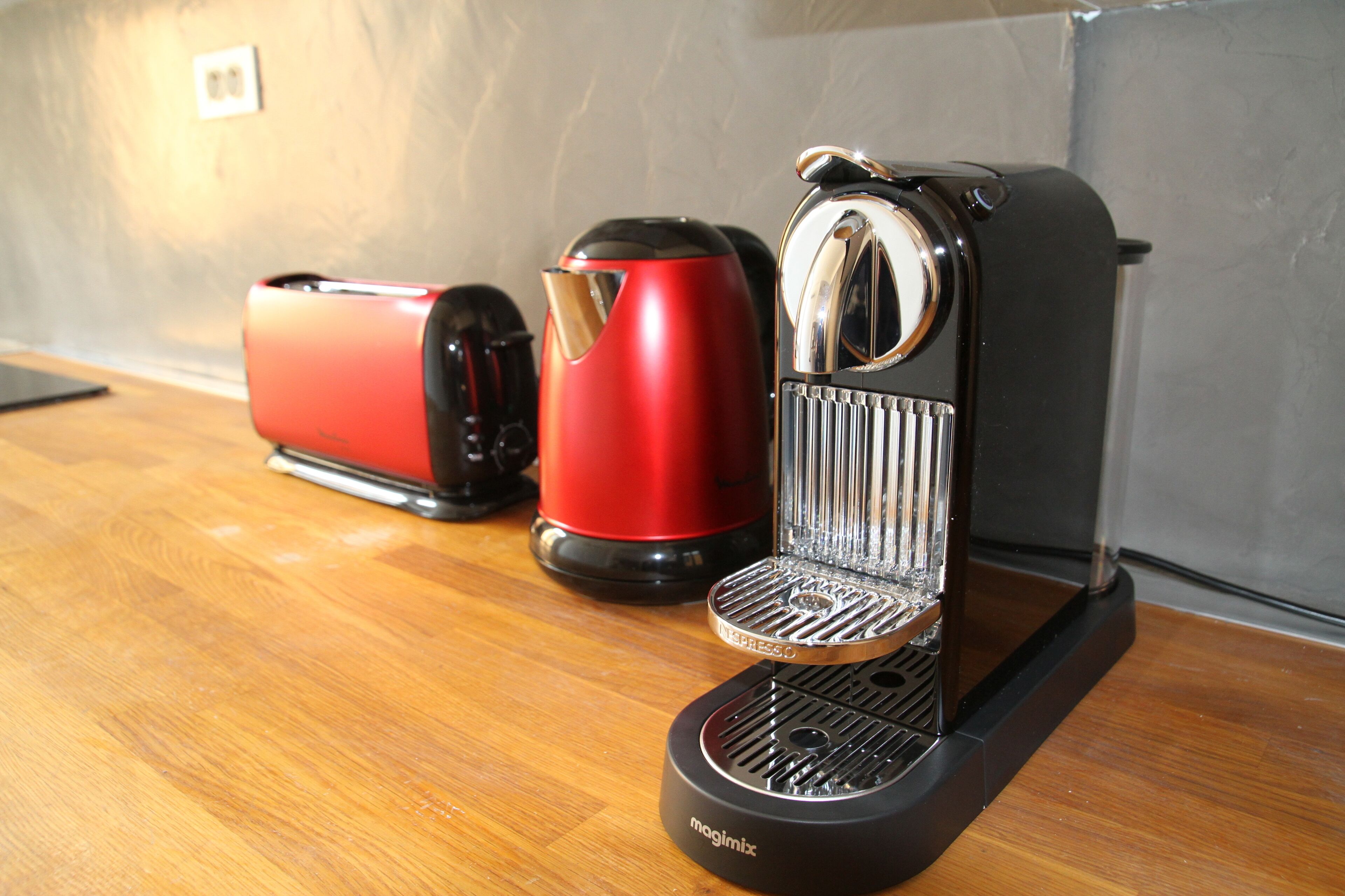 A coffee maker on a wooden countertop with a red and black coffee pot beside it.
