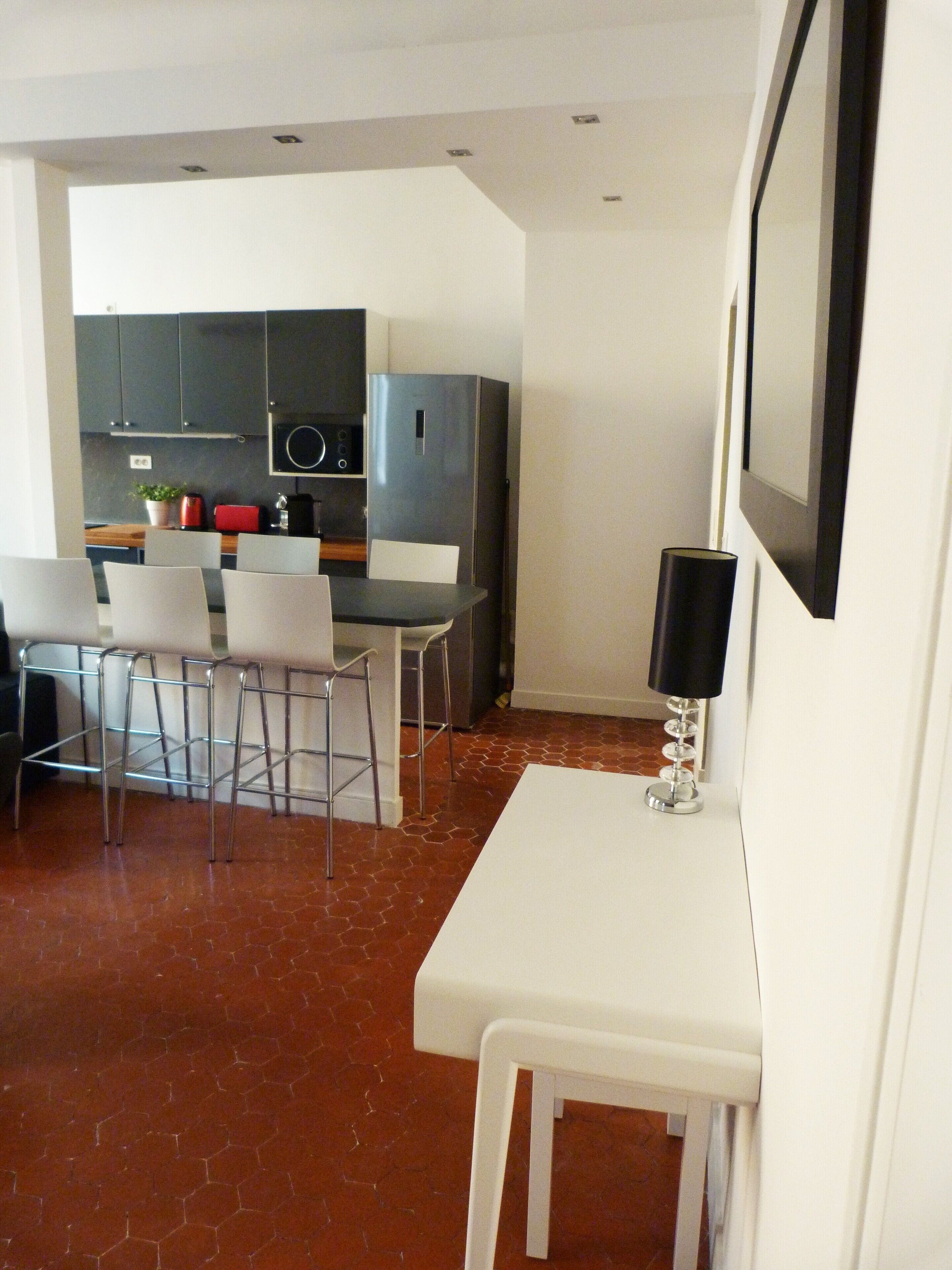 A modern kitchen with grey cabinets, a white dining table with four chairs, and a black floor lamp.