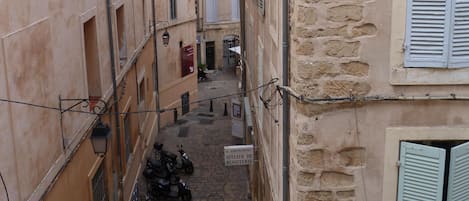 Un callejón estrecho flanqueado por edificios, una fila de scooters estacionados y un letrero que indica una panadería.