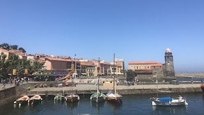 A coastal town with a historic tower, a marina with small boats, and a promenade with people and outdoor seating. - Collioure new air-conditioned apartment with private parking  (Collioure)