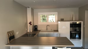 A modern kitchen with a central island, a built-in oven, and a window with a view of greenery. - Collioure new air-conditioned apartment with private parking  (Collioure)