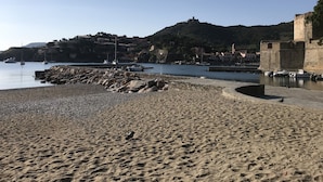 A beach with a rocky shoreline, boats in the water, and buildings on a hillside in the background. - Collioure new air-conditioned apartment with private parking  (Collioure)