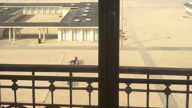 A beach view from a balcony with a metal railing, a sandy beach, a building with a flat roof, and the ocean in the background. - Trouville-sur-mer feet in the water (Trouville-Sur-Mer)