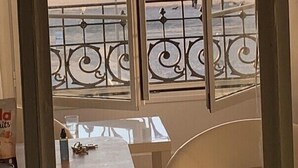 A balcony with a view of the beach, a table, and a chair. - Trouville-sur-mer feet in the water (Trouville-Sur-Mer)