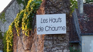 A stone sign with 'Les Hauts de Chaume' written on it, surrounded by greenery and flowers.