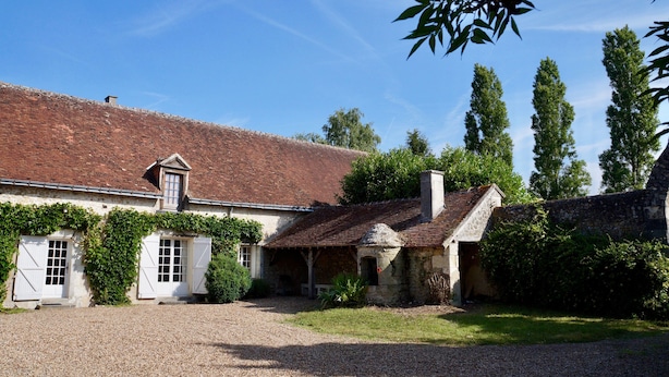 A traditional stone building with a tiled roof, a gravel driveway, and surrounding greenery.