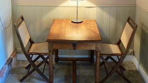 A dining area with a table and two chairs, a painting on the wall, and a lamp on the table.