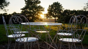 A metal outdoor table and chairs set in a garden with trees and a sunset in the background.