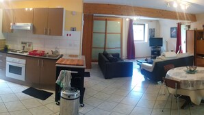 Una cocina moderna con estufa, horno y lavaplatos, un comedor con mesa y sillas, un sofá y televisor en la sala.
