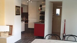 A compact kitchen with white cabinets, a red countertop, and a tiled floor. There is a dining area with a marble table and chairs. - Independent apartment in villa, in the pines overlooking the sea. (Ensuès-La-Redonne)