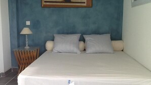 A bed with a white mattress, two pillows, and a wooden nightstand with a lamp. - Independent apartment in villa, in the pines overlooking the sea. (Ensuès-La-Redonne)