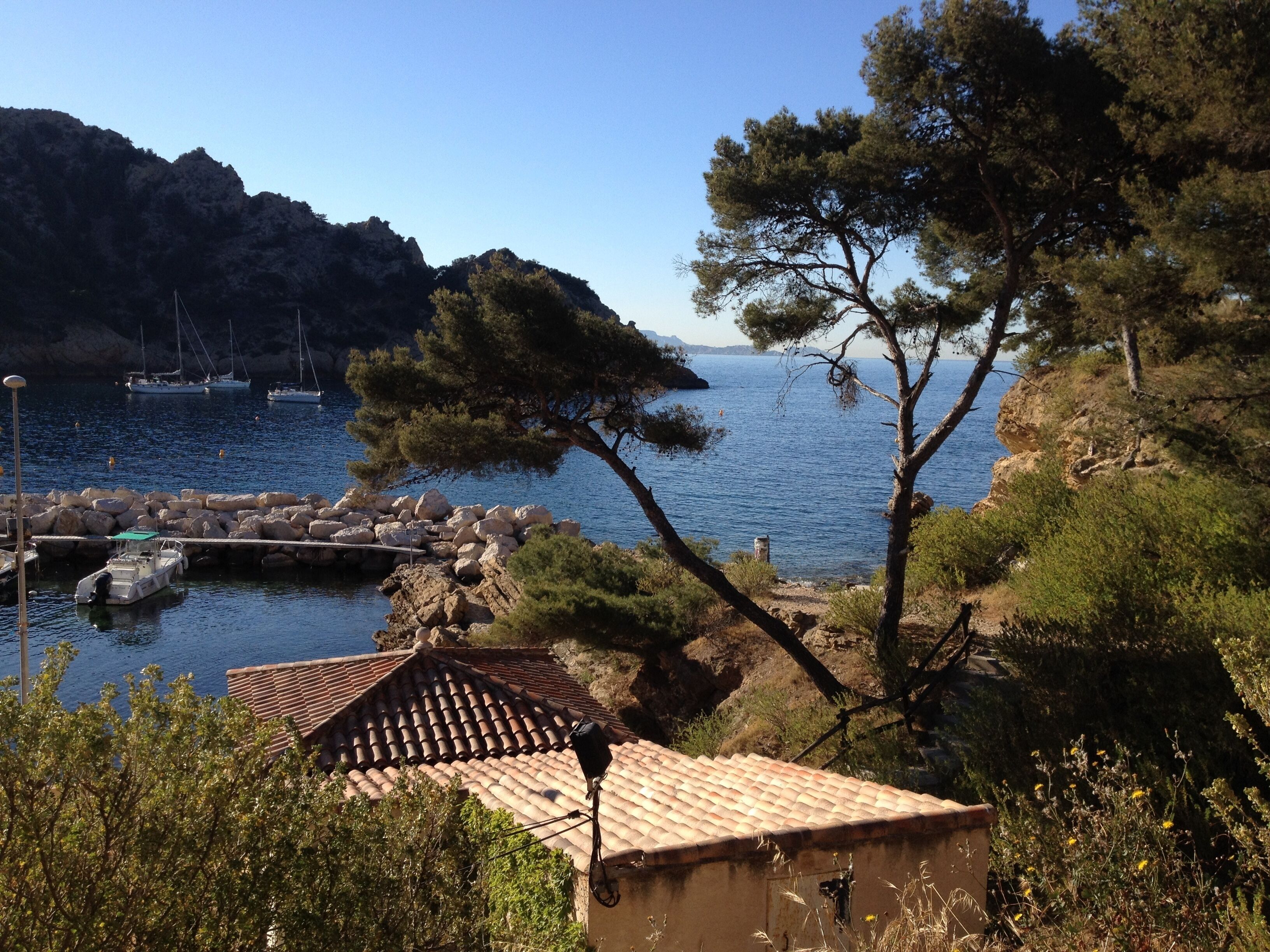 A coastal scene with rocky terrain, a small building with a tiled roof, and boats in the water.