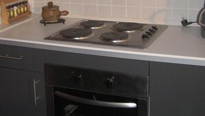 Een keuken met een gasfornuis, oven en een klein houten rek met potten.