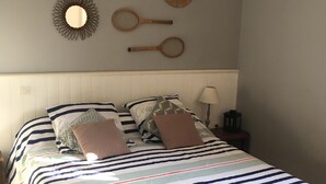 Ein Schlafzimmer mit gestreifter Bettdecke, einem weißen Kopfteil und Wanddekoration, darunter ein Spiegel in Sonnenform und Tennisraketen.