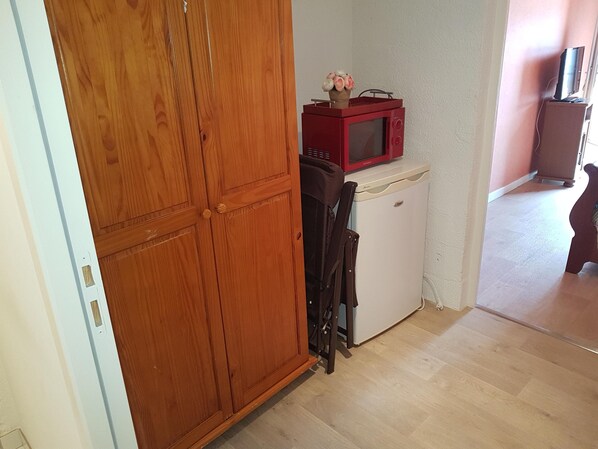 A compact kitchen with a wooden wardrobe, a white refrigerator, and a red microwave.