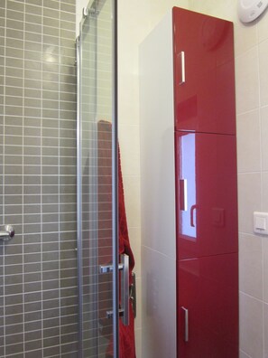 A bathroom with a glass shower enclosure, a red cabinet, and a white tiled wall. - Charming house, 3***, 400m from the beach, GR34 and thalasso baths (Concarneau)