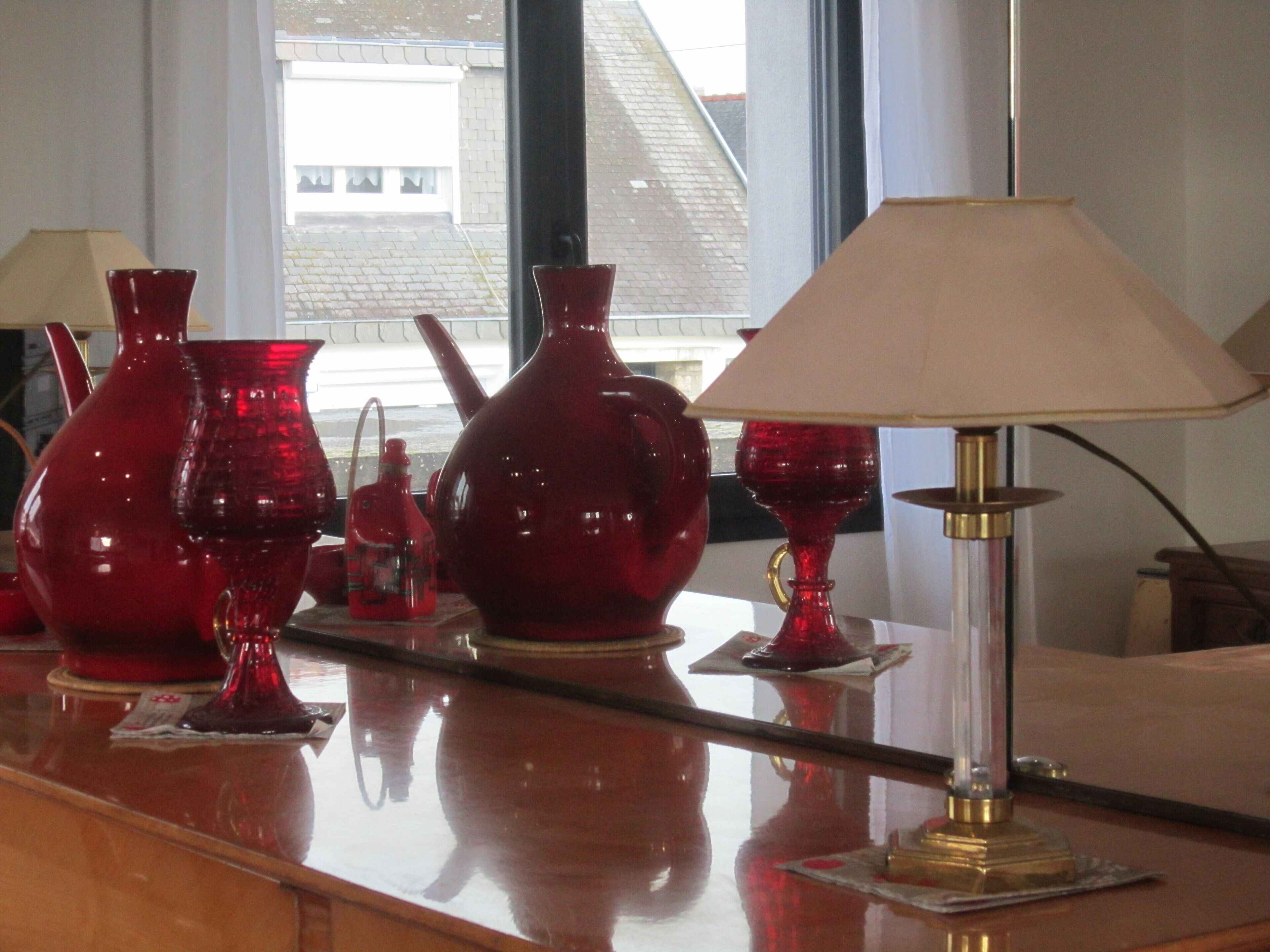 A room with a wooden counter displaying red glassware and a table lamp.