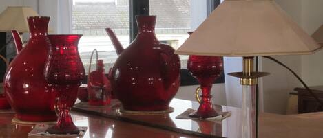 A room with a wooden counter displaying red glassware and a table lamp.