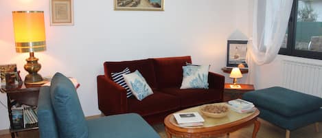 A living room with a red sofa, blue armchairs, a wooden coffee table, and a bookshelf.