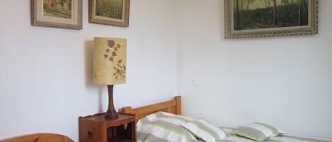 Un dormitorio con dos camas individuales, una mesita de noche con lámpara y dos cuadros en la pared.