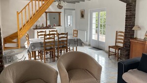 A dining area with a wooden staircase, a table set with chairs, and a view of the outdoors through a door.