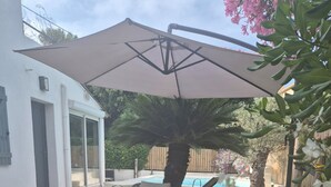 Een achtertuin met kunstgras, twee rieten stoelen, een grote parasol en een zwembad.