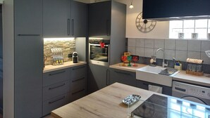 Een moderne keuken met grijze kastjes, een houten aanrechtblad, een inbouwoven en een klok aan de muur.
