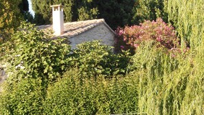 Ein Haus mit Steindeckung und Schornstein, umgeben von üppigem Grün und blühendem Gebüsch.