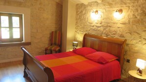 Ein Schlafzimmer mit Steinwand, einem hölzernen Bett, einem Stuhl und einem Fenster.