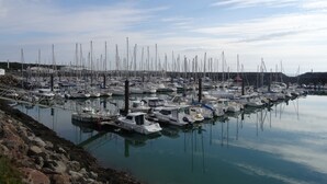 A marina with numerous boats docked, calm water, and a rocky shoreline.