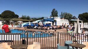 A pool area with lounge chairs and umbrellas, a lifeguard in a red shirt, and a water slide in the background.