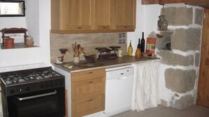 A kitchen with wooden cabinets, a stove, a dishwasher, and a stone wall. - Longueville Castle, the Thines Malarce valley on Thines (Malarce-Sur-La-Thines)
