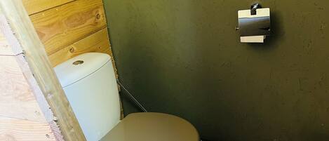 A small, compact bathroom with a toilet, a trash bin, and a wooden wall.