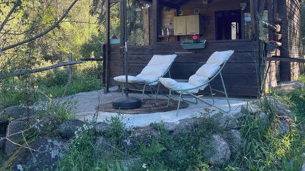 A wooden cabin with a patio, two white lounge chairs, and a large umbrella. - LITTLE QUIET CORNER FOR NATURE LOVERS ... (Olivese)