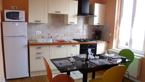A compact kitchen with a refrigerator, microwave, stove, and sink. There are two chairs and a table with a placemat. - Apartment 1 to 2 people in Cayeux-sur-mer in the Baie de Somme (Cayeux-Sur-Mer)