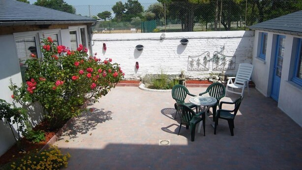 A patio area with a table and chairs, a white brick wall, and a garden with red and yellow flowers. - Apartment 1 to 2 people in Cayeux-sur-mer in the Baie de Somme (Cayeux-Sur-Mer)