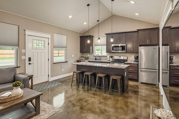 A modern kitchen with dark wood cabinets, stainless steel appliances, and a central island with bar stools. - Stoneridge Place Cottage #1 - Vacation or Executive Retreat 1Br 1Ba Garage! (Wasilla)