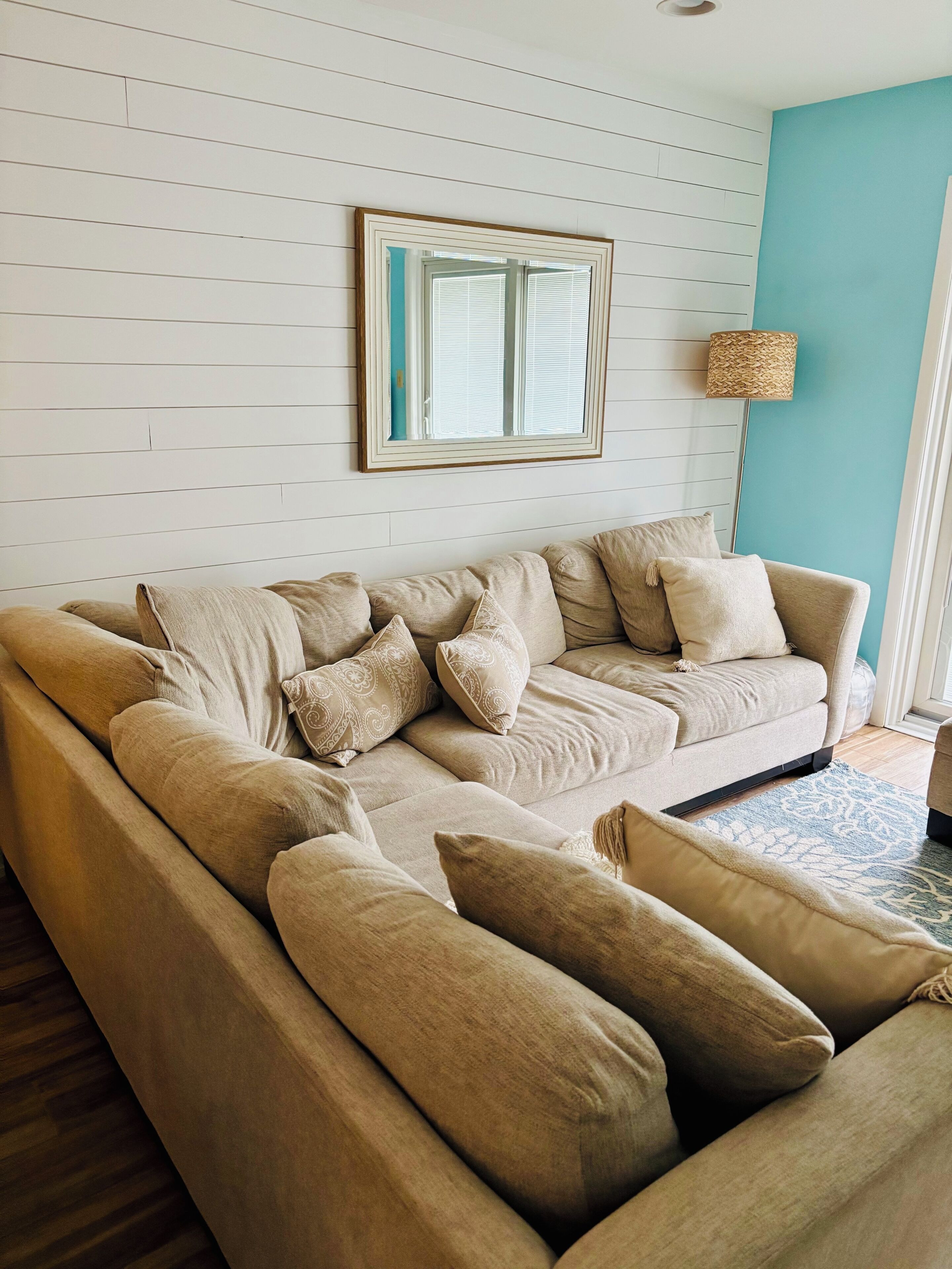A modern living room with a beige sectional sofa, a large mirror, and a floor lamp.