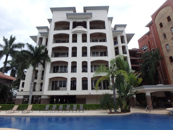 A multi-story hotel with balconies, a swimming pool, and palm trees.