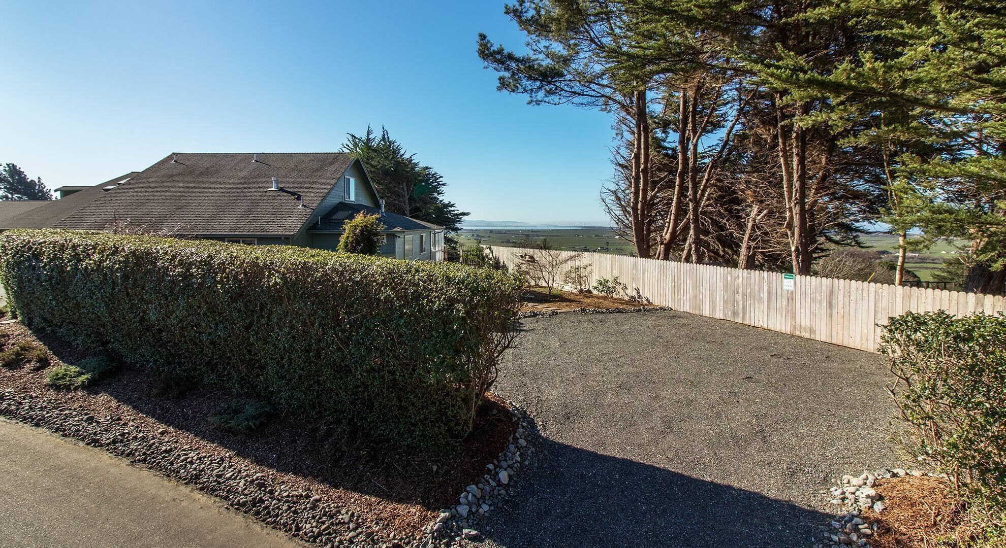 A residential driveway with a gravel path, a wooden fence, and a hedge.