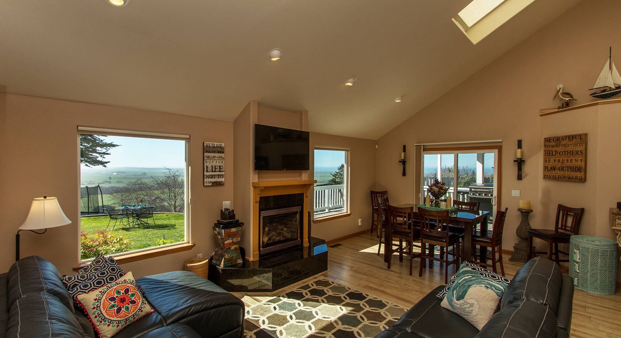 A spacious living room with a fireplace, a dining area, and large windows offering a view of the outdoors.