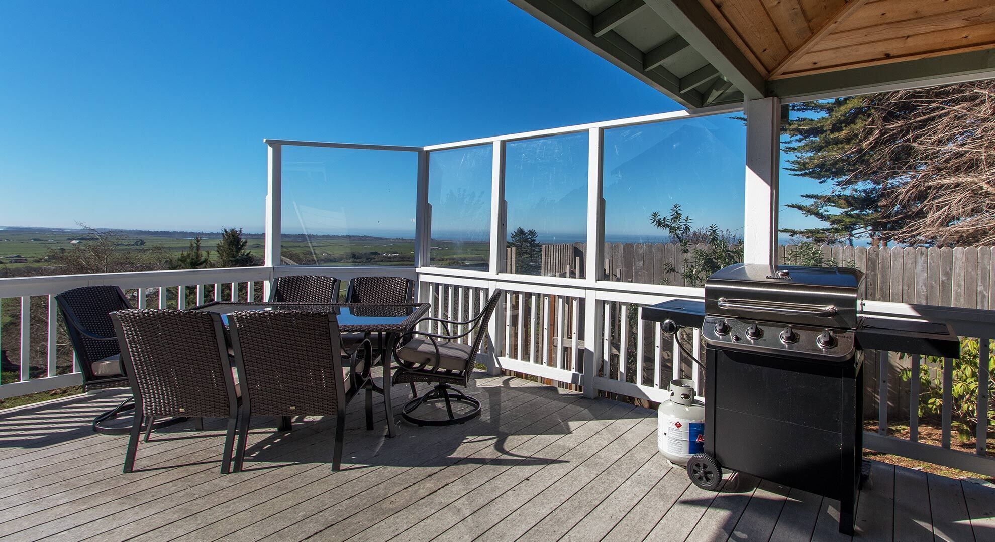 Une terrasse extérieure couverte, équipée d’une table et de chaises, d’un barbecue et offrant une vue sur le paysage.