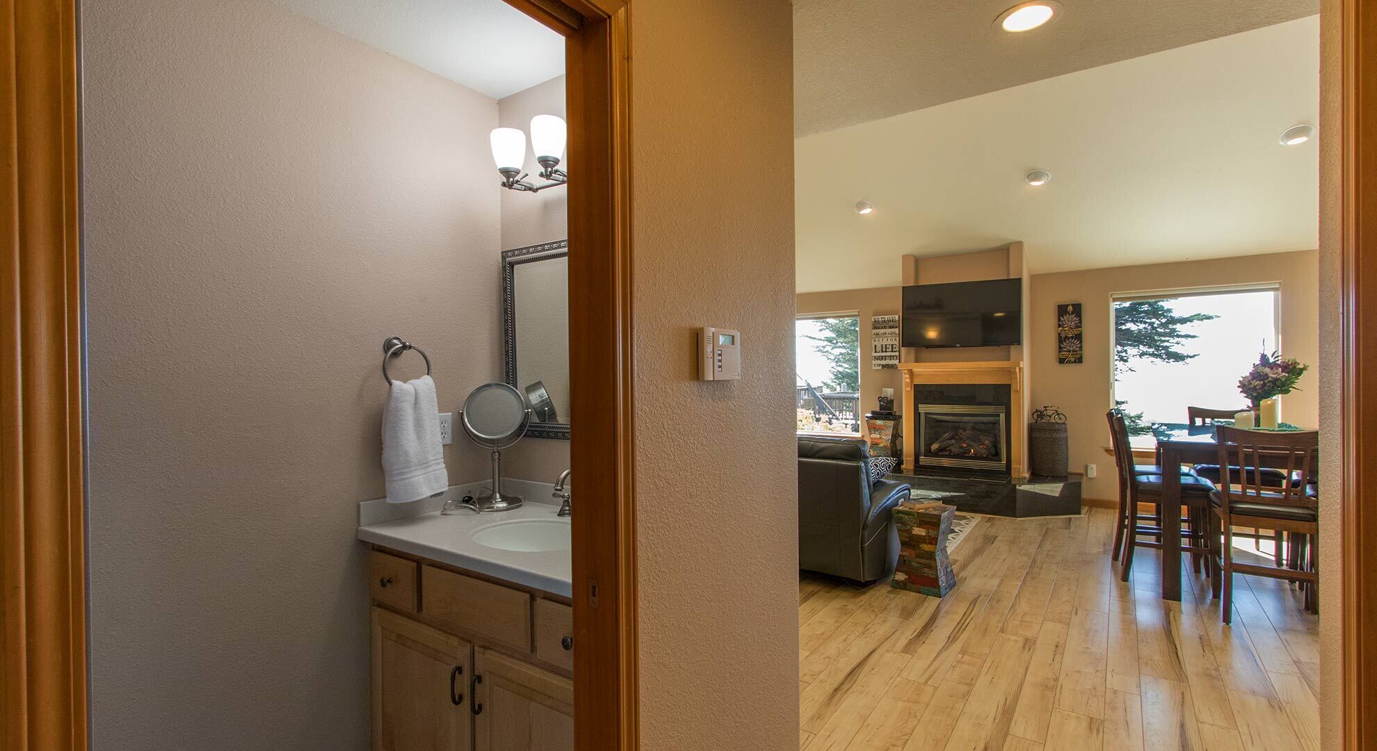A bathroom with a sink, mirror, and towel rack. The living room features a fireplace, TV, and dining area with chairs.