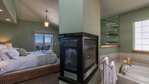 Une chambre à coucher avec un lit, une cheminée, une salle de bain avec une baignoire et une grande fenêtre.
