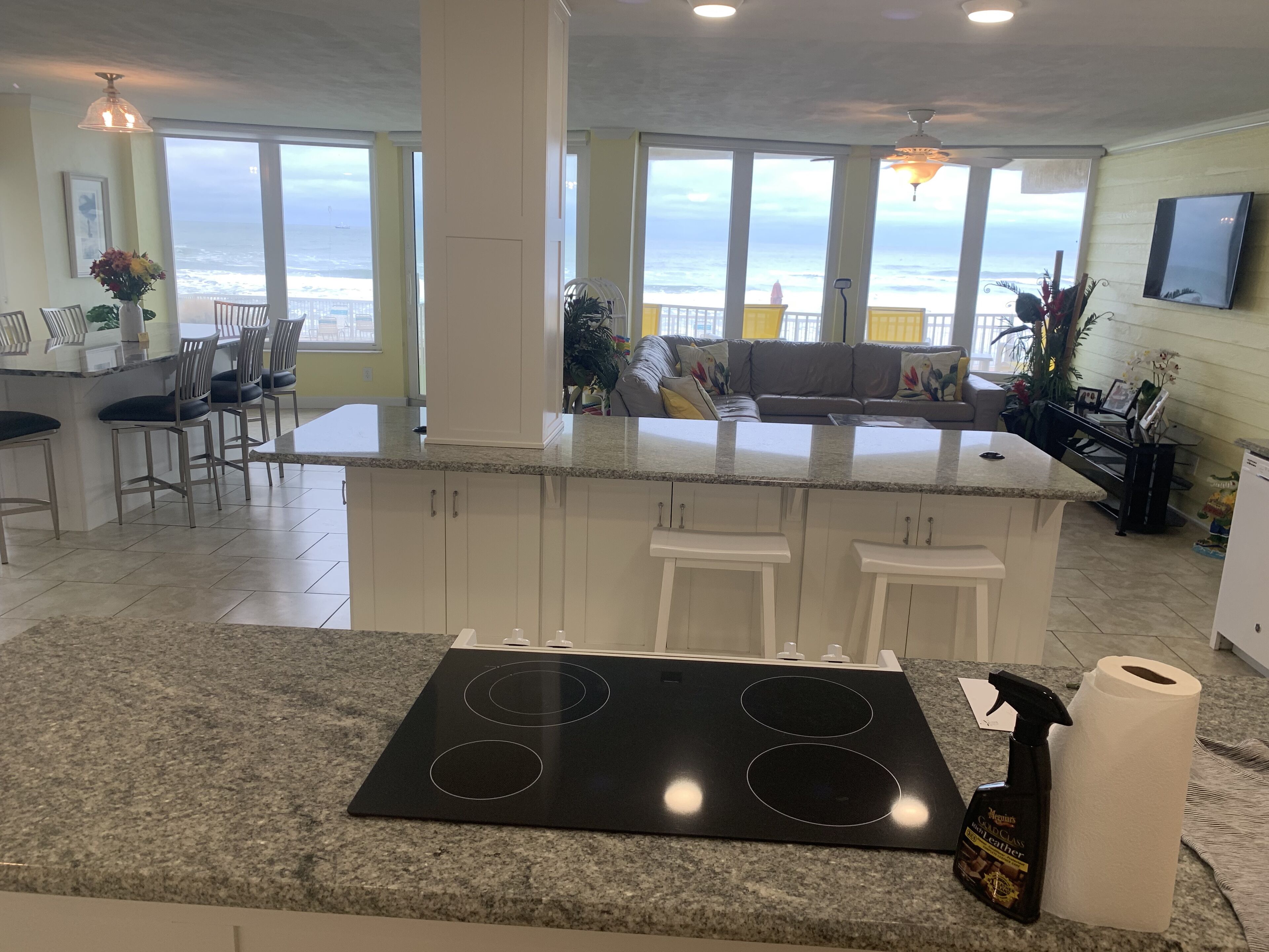 A modern kitchen with a central island, large windows overlooking the ocean, and a dining area with chairs and a table.