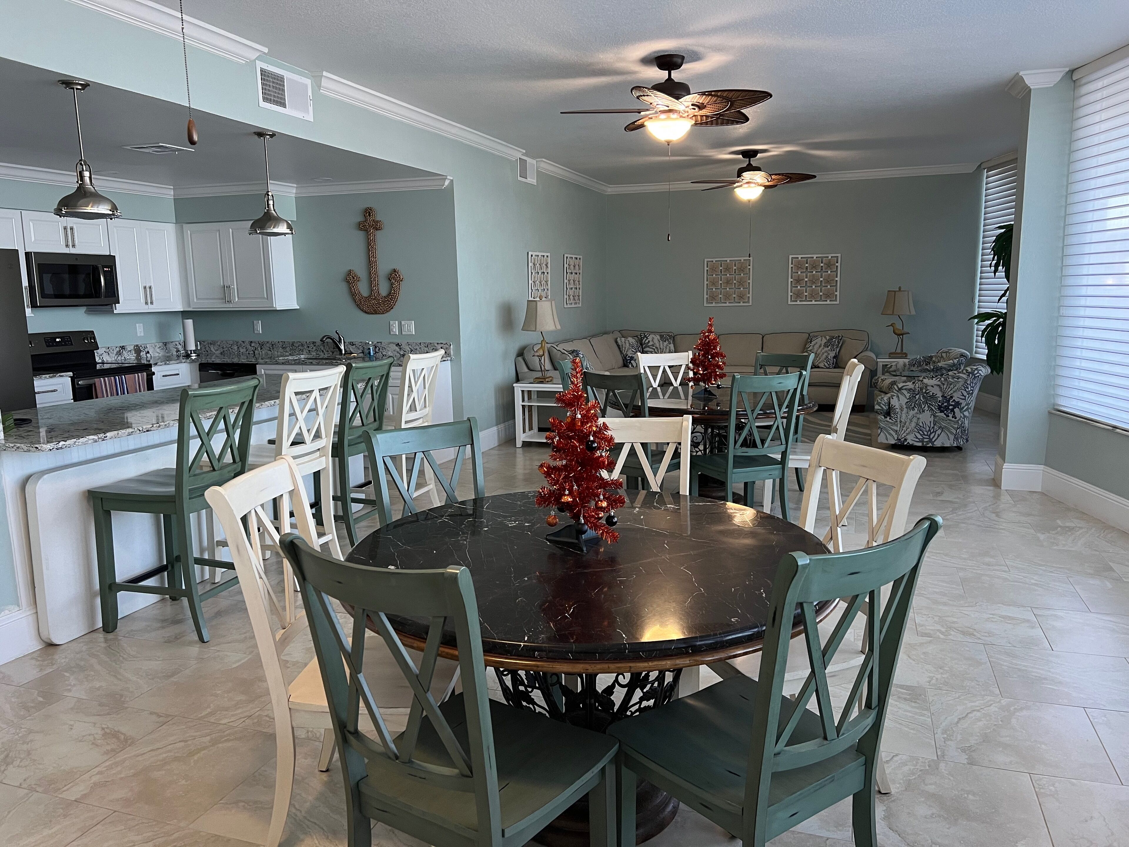 A spacious living area with a dining table surrounded by chairs, a kitchen with white cabinets, and a ceiling fan.