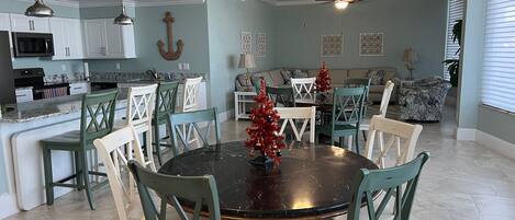 A spacious living area with a dining table surrounded by chairs, a kitchen with white cabinets, and a ceiling fan.